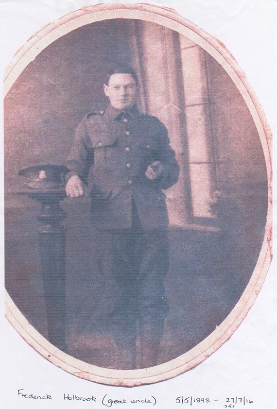 Studio photographic portrait of a young man in army uniform standing between a window on his left and pedestal with his service cap on it to his right. A cane under his left arm.