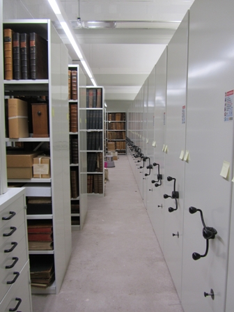 image of an archive strongroom with fixed and mobile racking and volumes visible on the shelves