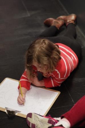 An image of a child laying on the floor and drawing a map