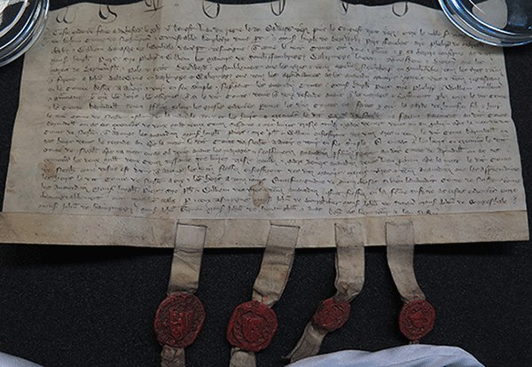 A document written in French on parchment with four small red wax seals appended that grants manors in Essex to four men, 1359
