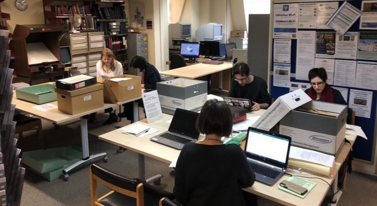 A picture of people working on computers with archive boxes on tables