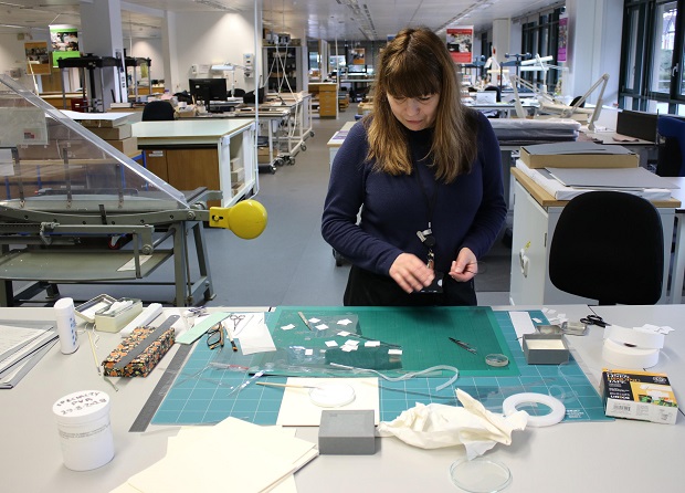 Conservator Jamie Beveridge is shown at work in the Collection Care department preparing materials to mount documents on 'museum board' so that they can be displayed in the Cold War exhibition
