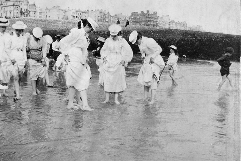 An old black and white photograph of a group of fully-clothed ladies paddling.