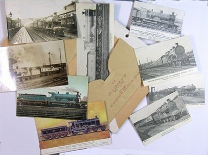 Nine postcards and photographs with images of trains laid out around the envelope that contained them, ready to be catalogued by the volunteers