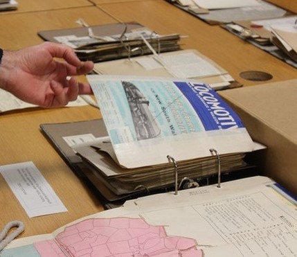 A binder from the collection full of railway ephemera with a person's hand turning a page showing a magazine with the title Locomotive