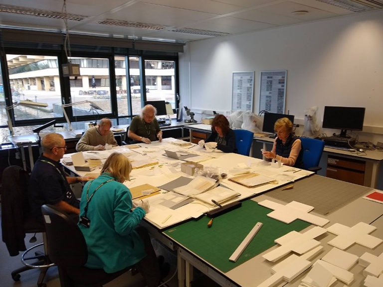 Part of the group of volunteers working on rehousing films and negatives, seated around a table in a room at The National Archives.