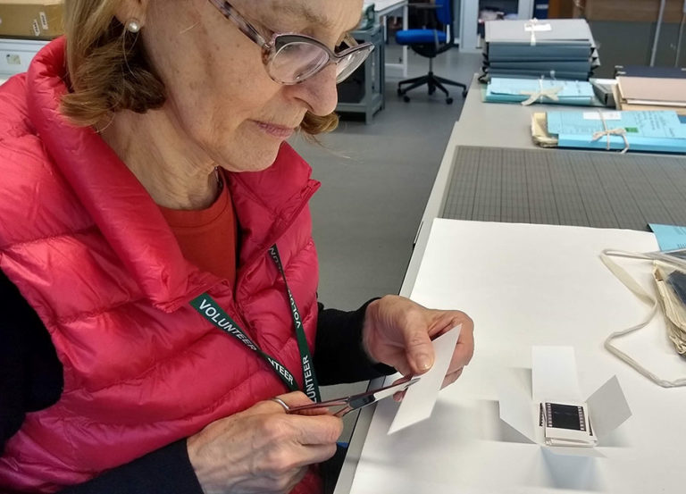 A volunteer working meticulously to rehouse a group of negatives in a file.