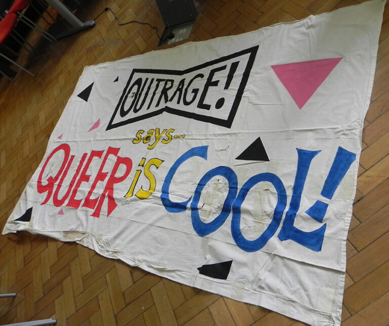 Large banner that says 'Outrage! says Queer is cool!'.