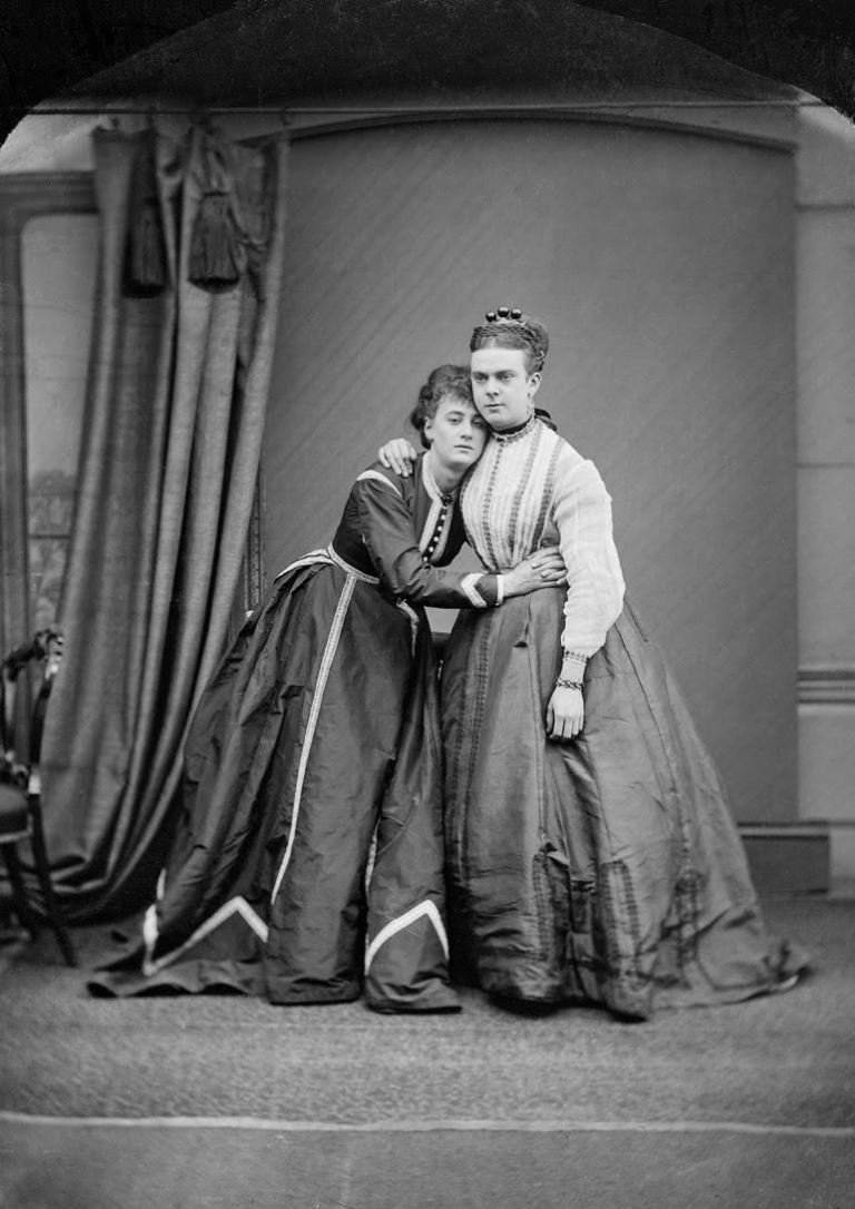 Black and white portrait photograph of Fanny and Stella taken in 1869. They are standing together holding on to one another.