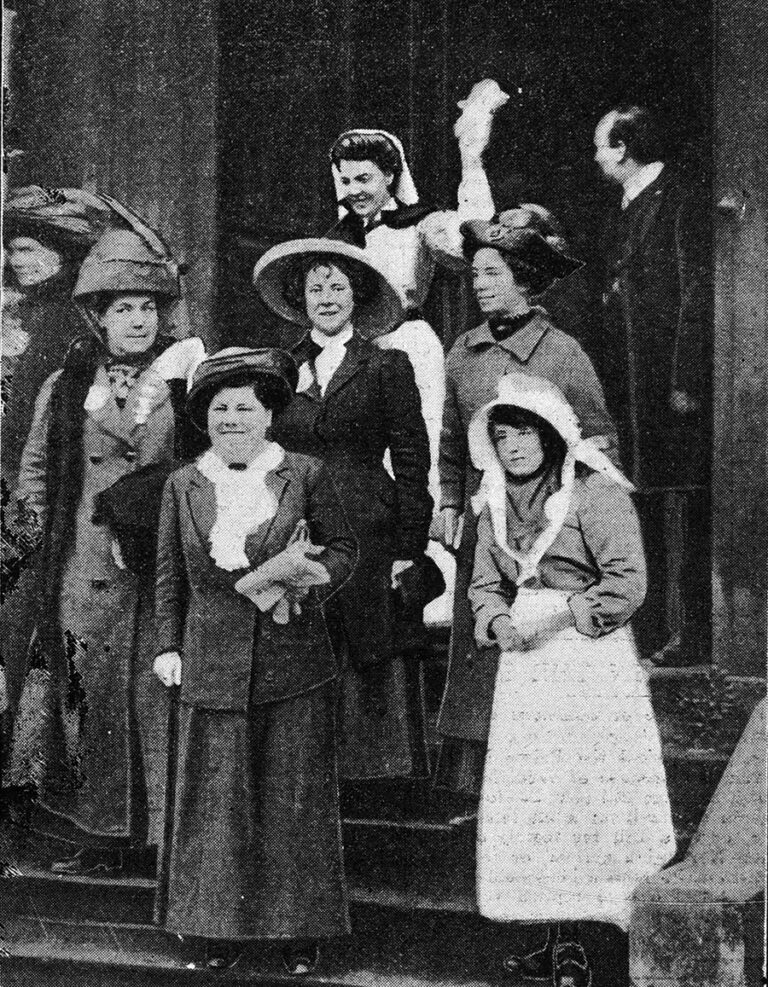 A group of seven suffragettes emerging from a building looking triumphant.