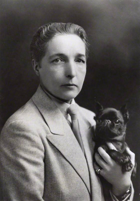 Black and white photograph of author Radclyffe Hall holding a small black dog.