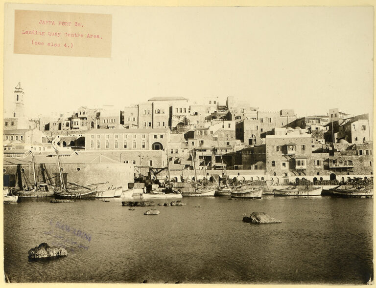 Sepia tinted photograph of Jaffa Port, Palestine, in the 1920s. The scene is a busy port with numerous ships and boats overlooked by the town's buildings. The British administration undertook the development of Jaffa as a modern port during the 1920s and 1930s.