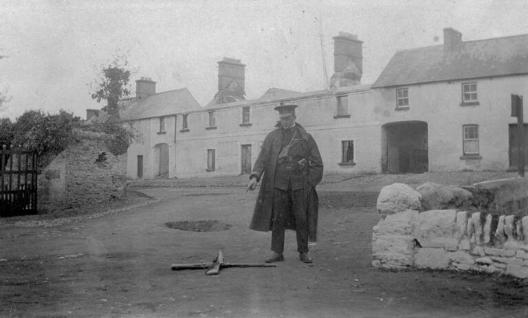 RIC policeman standing in front of a large building points to the spot were a constable was wounded.