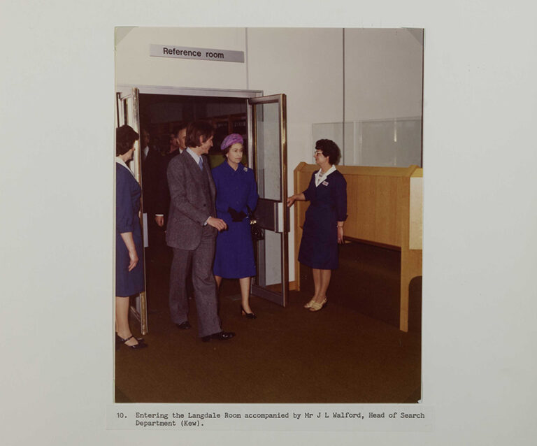 Her Majesty The Queen enters a room at The National Archives accompanied by Mr J L Walford from the Archives as two women hold the door open for them.