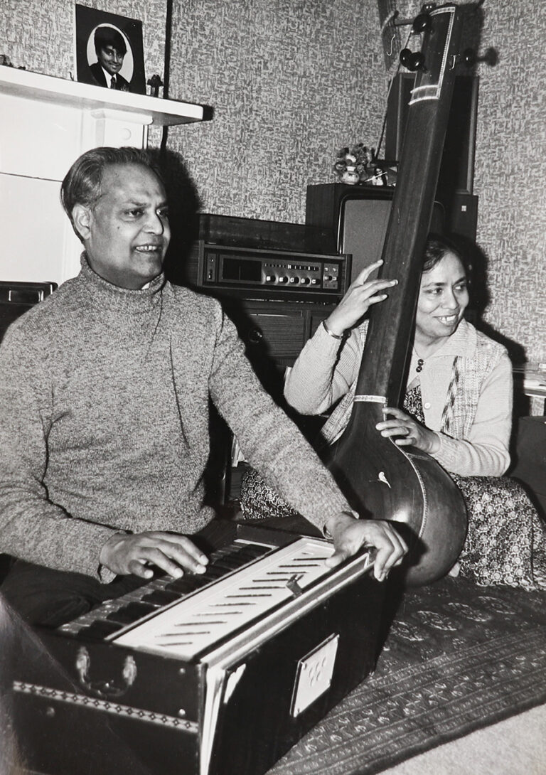 A man and a woman, who are Mr and Mrs Iqbal, are shown playing Indian musical instruments in a room in their house.