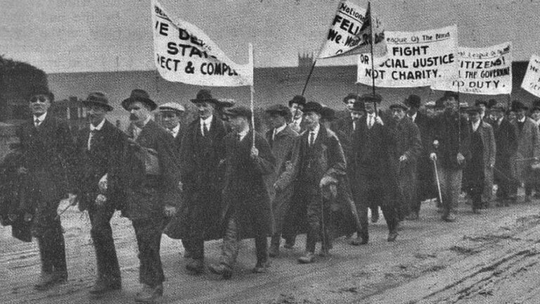 A group of men walk in protest holding banners with slogans on.