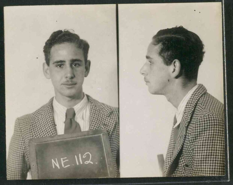 Irwin Sanders is photographed both facing the camera and in side profile. He holds a small black board on which NE 112 is written in white chalk.