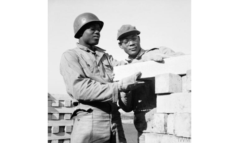 Two Black GIs in uniform in the process of building a wall.