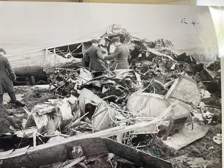 Officers in uniform surrounded by the debris of a crashed plane.