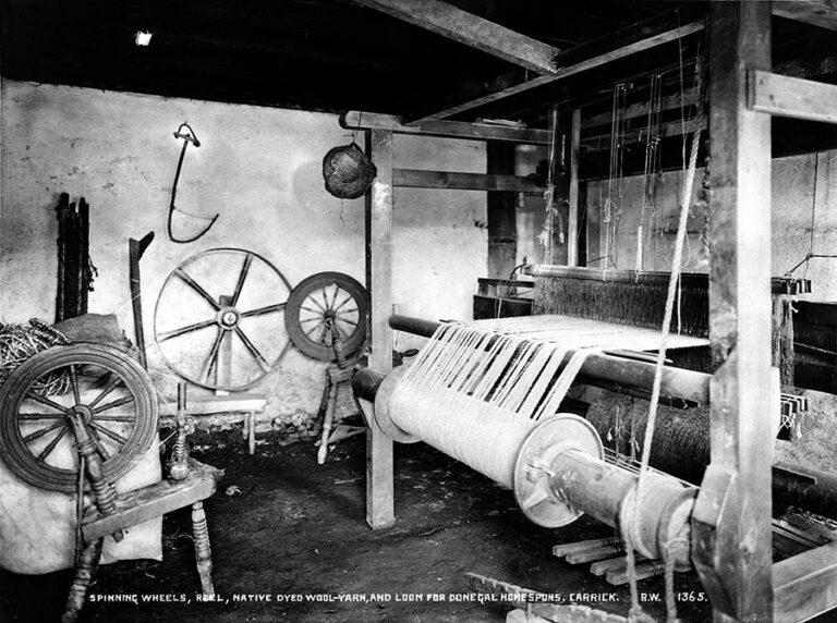 A room filled with equipment for spinning wool. The room is dominated by a large loom. Wheels are shown hanging on the wall.