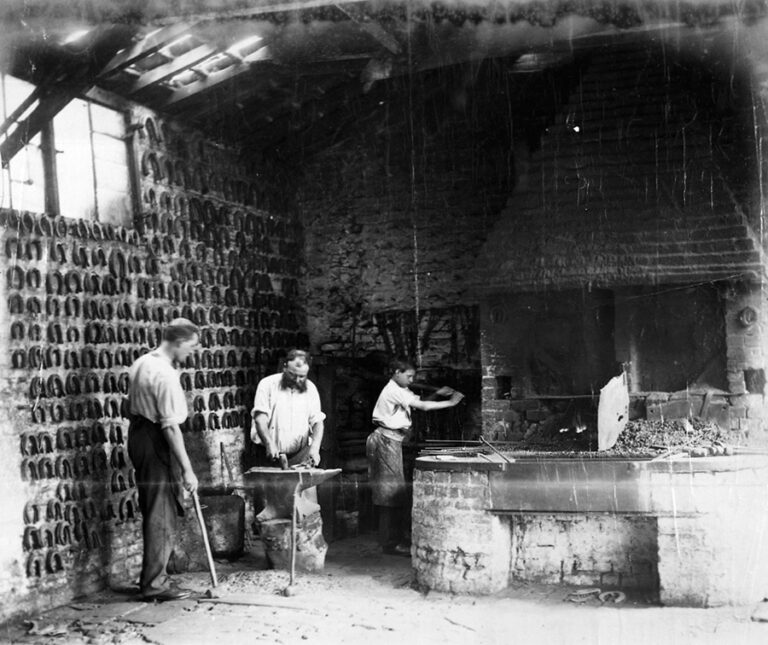 Three men, two blacksmiths and a younger apprentice, work in a blacksmith's forge making coins.