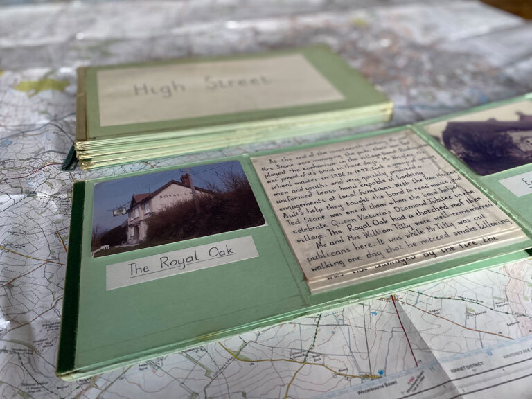 A small book lies open on top of a map. Pasted into the book are a photograph of a pub and hand-written notes