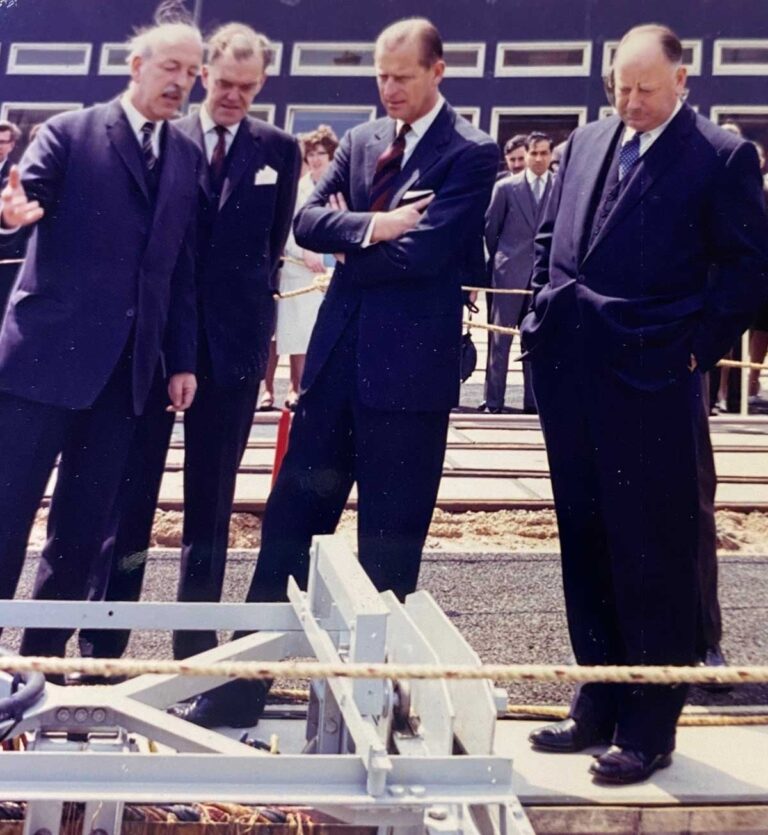 Photograph of four men in suits looking down at a piece of railway equipment.