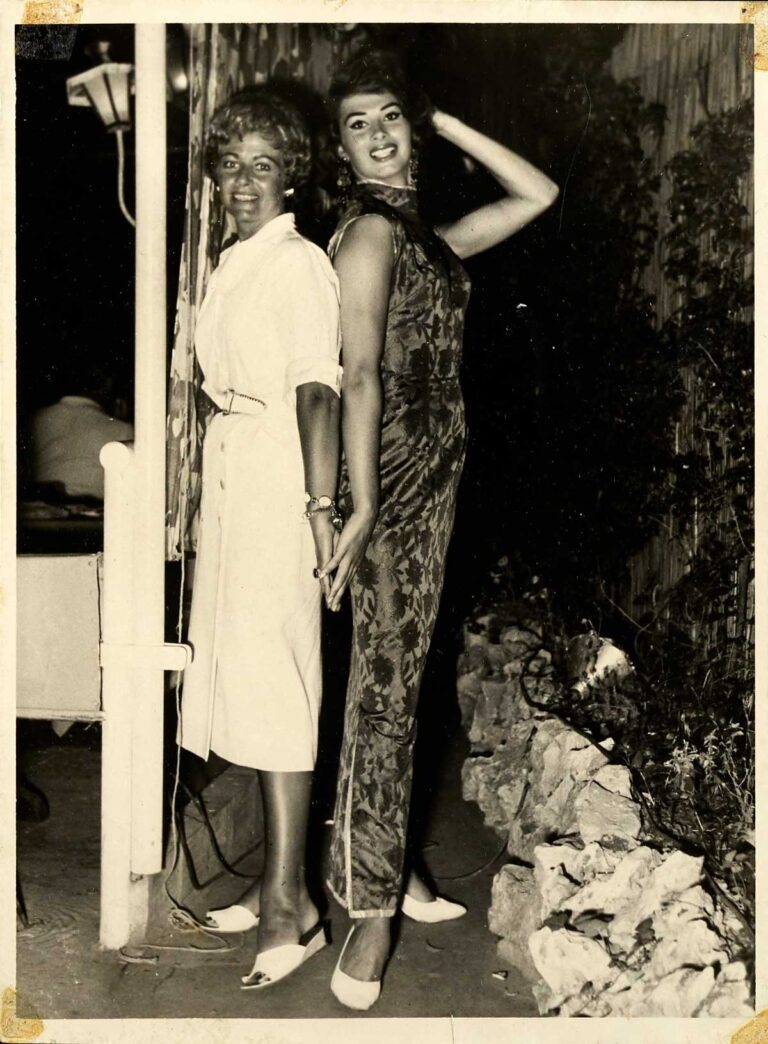 Two women in dresses standing back-to-back and smiling.