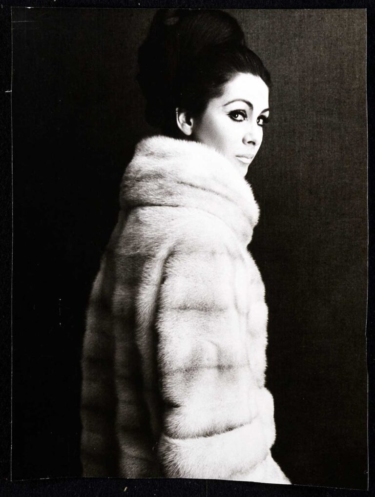 Modelling photo of a woman in a white fur coat turning to look seriously at the camera.
