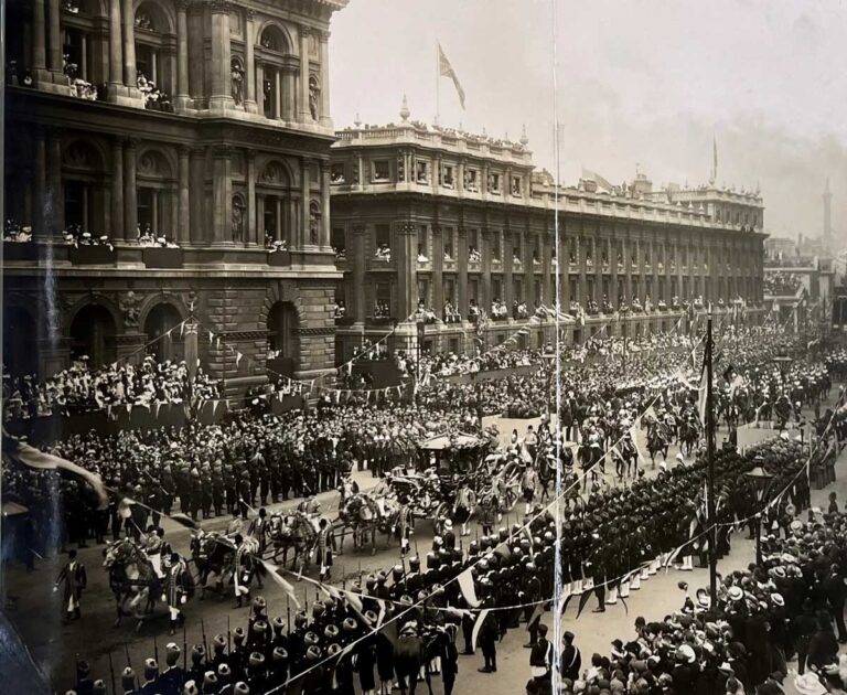 An ornate carriage pulled by four rows of two horses  is flanked by columns of soldiers on either side, watched by crowds of people.
