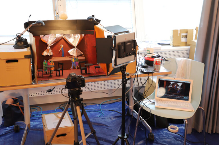 A stop-motion film set is setup on a desk with a camera and lights around it. 