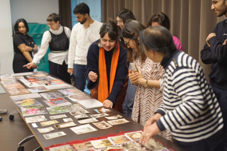 A group of people stood looking and discussing photos and pictures laid out on a table. 