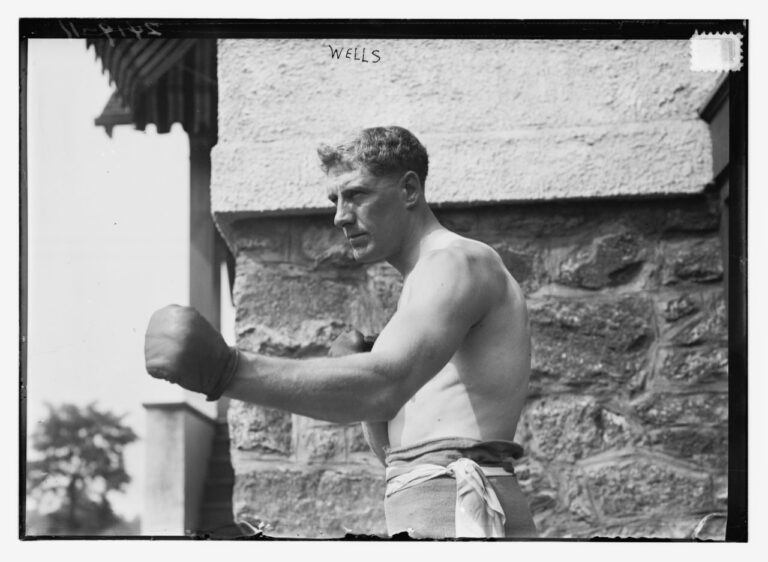 A topless, muscular man holds out a boxing-gloved-fist.