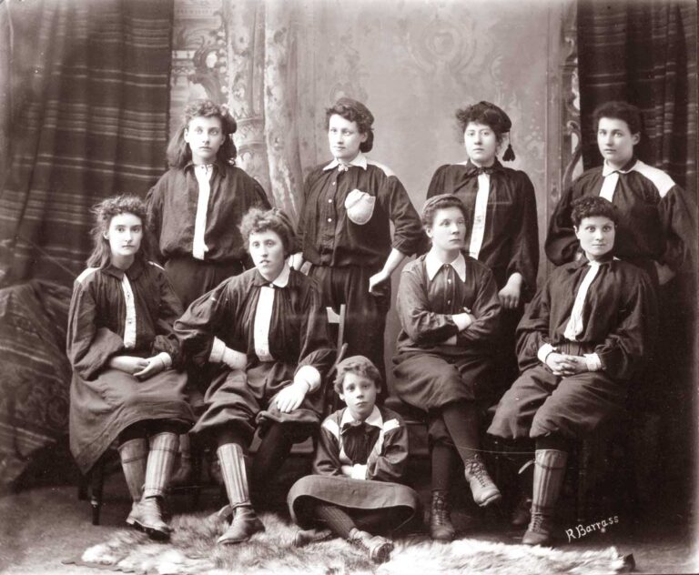 Nine young women wearing dark jerseys and shin pads pose with neutral expressions.
