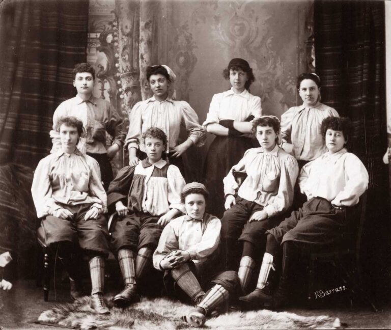 Nine young women wearing light jerseys and shin pads pose, as in the photo above, with neutral expressions.
