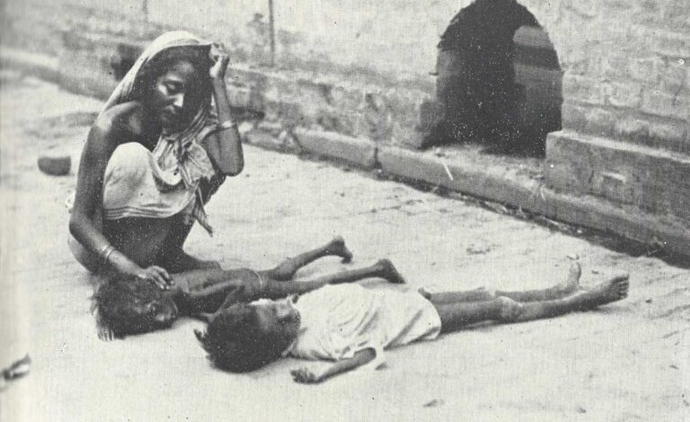 An adult wearing a headscarf and sari crouches with their hand on the back of an emaciated child that appears to be dead, lying next to another child in a similar position.