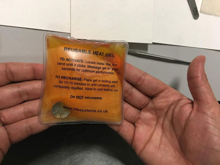 A pair of hands holding a square plastic pouch with the label 'reusable heat gel'. 