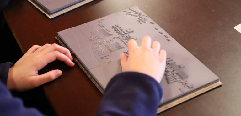 A student uses their hands to explore a tactile version of a Tudor battle map in which raised textures are used to represent two armies facing off.