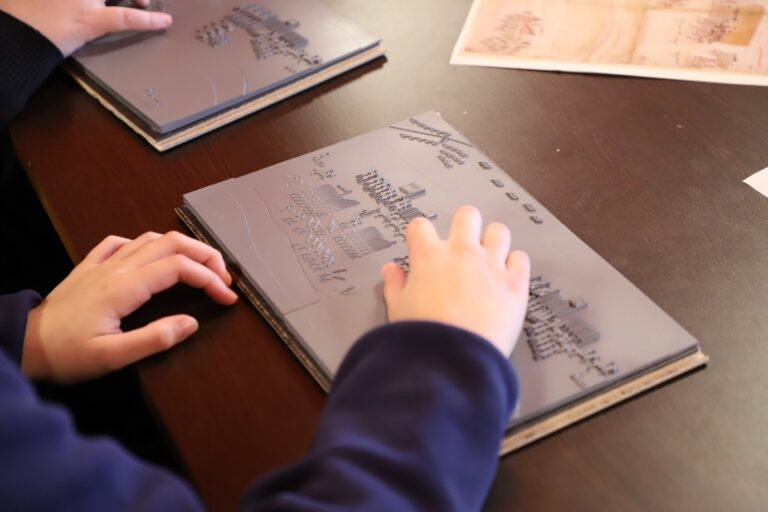 A student uses their hands to explore a tactile version of a Tudor battle map in which raised textures are used to represent two armies facing off.