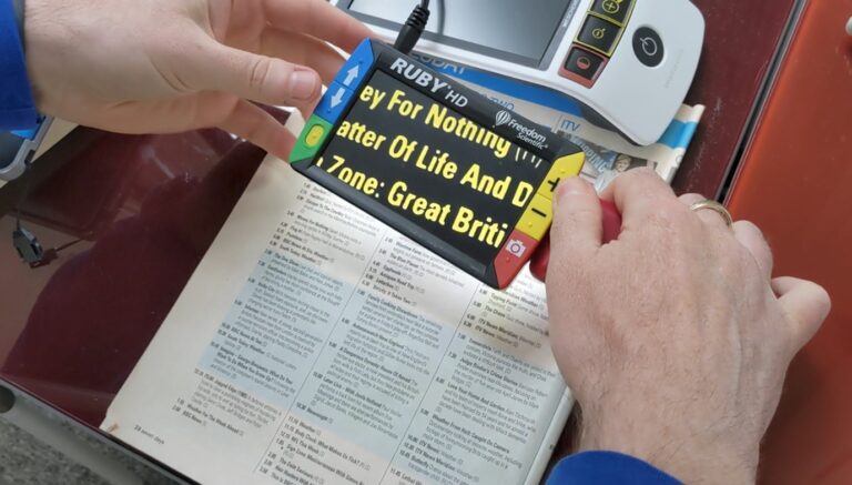 Person holding a small handheld electronic magnifier and using it to read text.