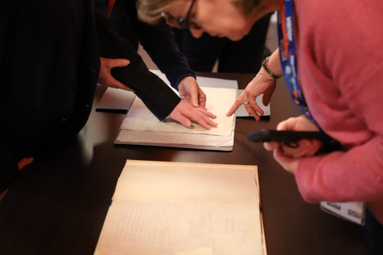 A student's hand is guided to touch a signature on a Tudor-era piece of parchment.