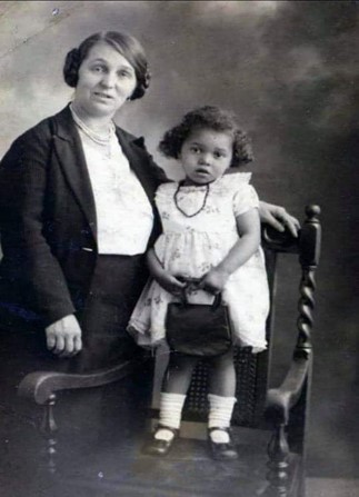 Black and white photo of a smartly dressed woman with straight hair in buns and her young daughter with very curly hair.