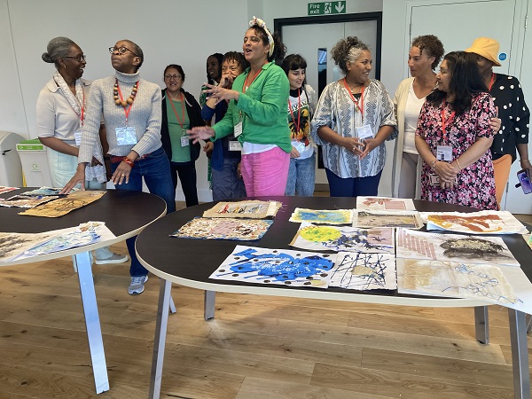 A group of people participating in a creative workshop at The National Archives. Their work is on a table in front of them. They are not looking at the camera but chatting.