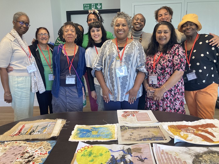 A group of people participating in a creative workshop at The National Archives. Their work is on a table in front of them. They are looking at the camera smiling. 