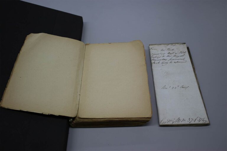 An open book made of paper. Alongside it is a rectangle piece of paper with handwriting on it. 