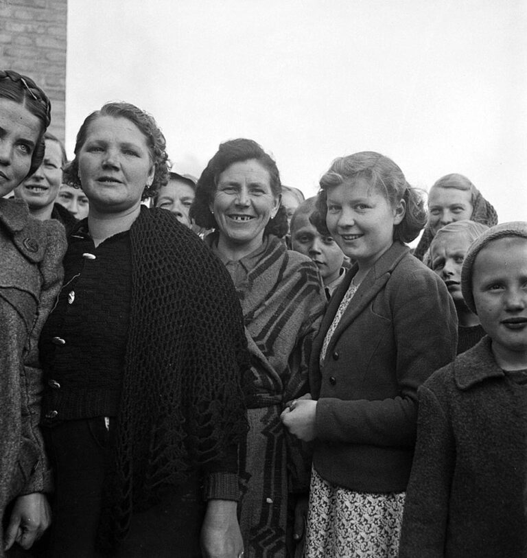 A black and white photograph of group of woman of different ages looking towards the photographer. Most pictured are smiling.