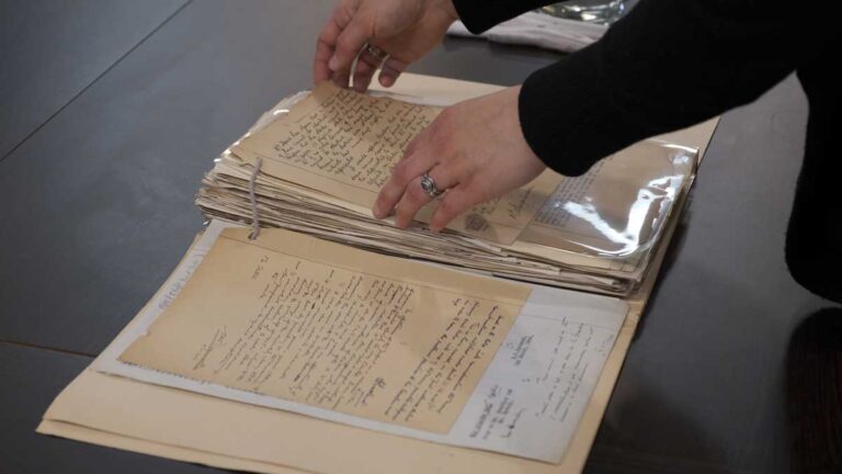 A person touches a handwritten note in a folder held together by a treasury tag.