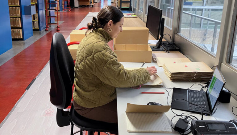 An employee of The National Archives going through documents in front of a laptop in the repository.